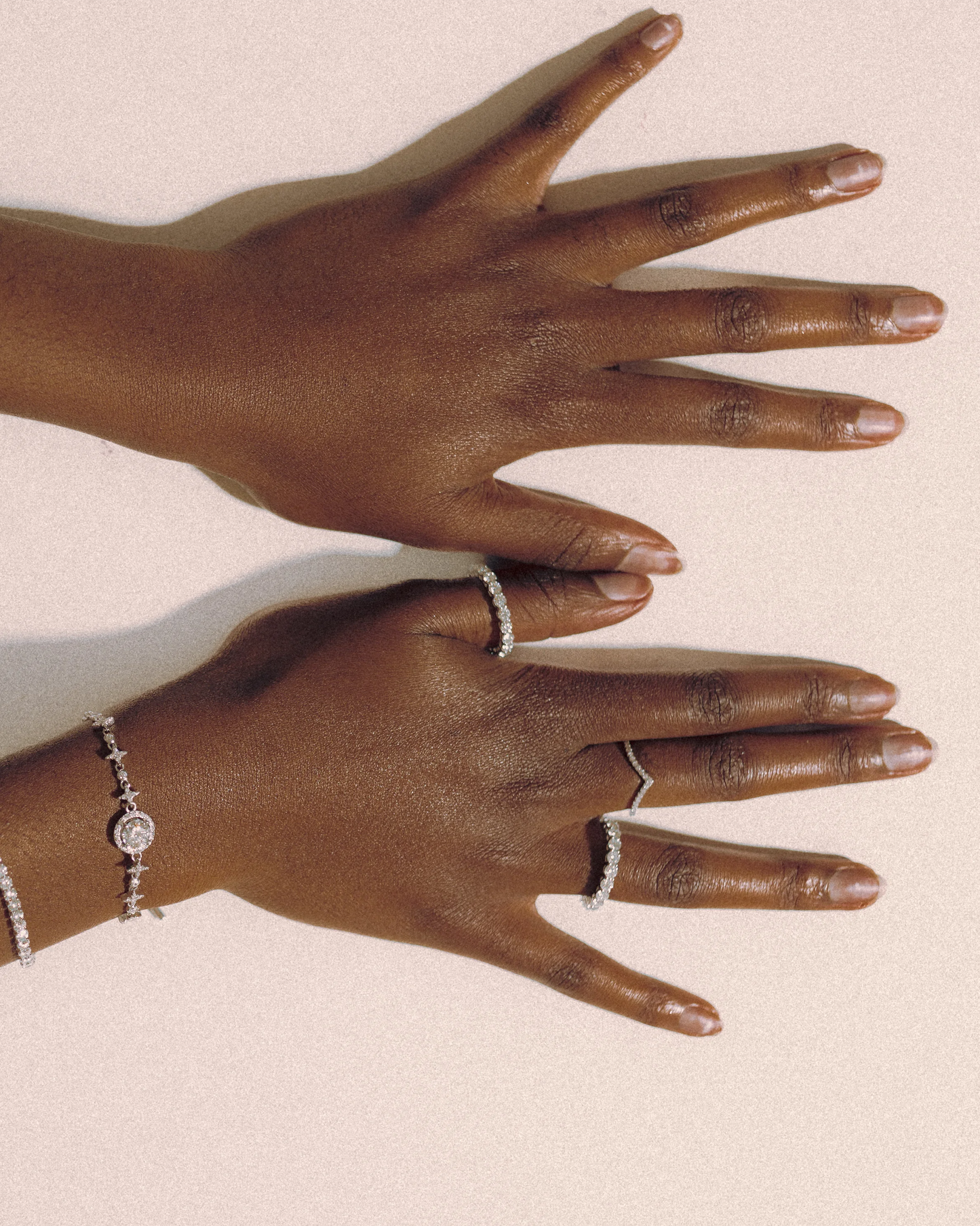 Top view of model’s hands showcasing Goldmacher Ethereal and Lynx moissanite rings, paired with Lyric and Celeste tennis bracelets in sterling silver