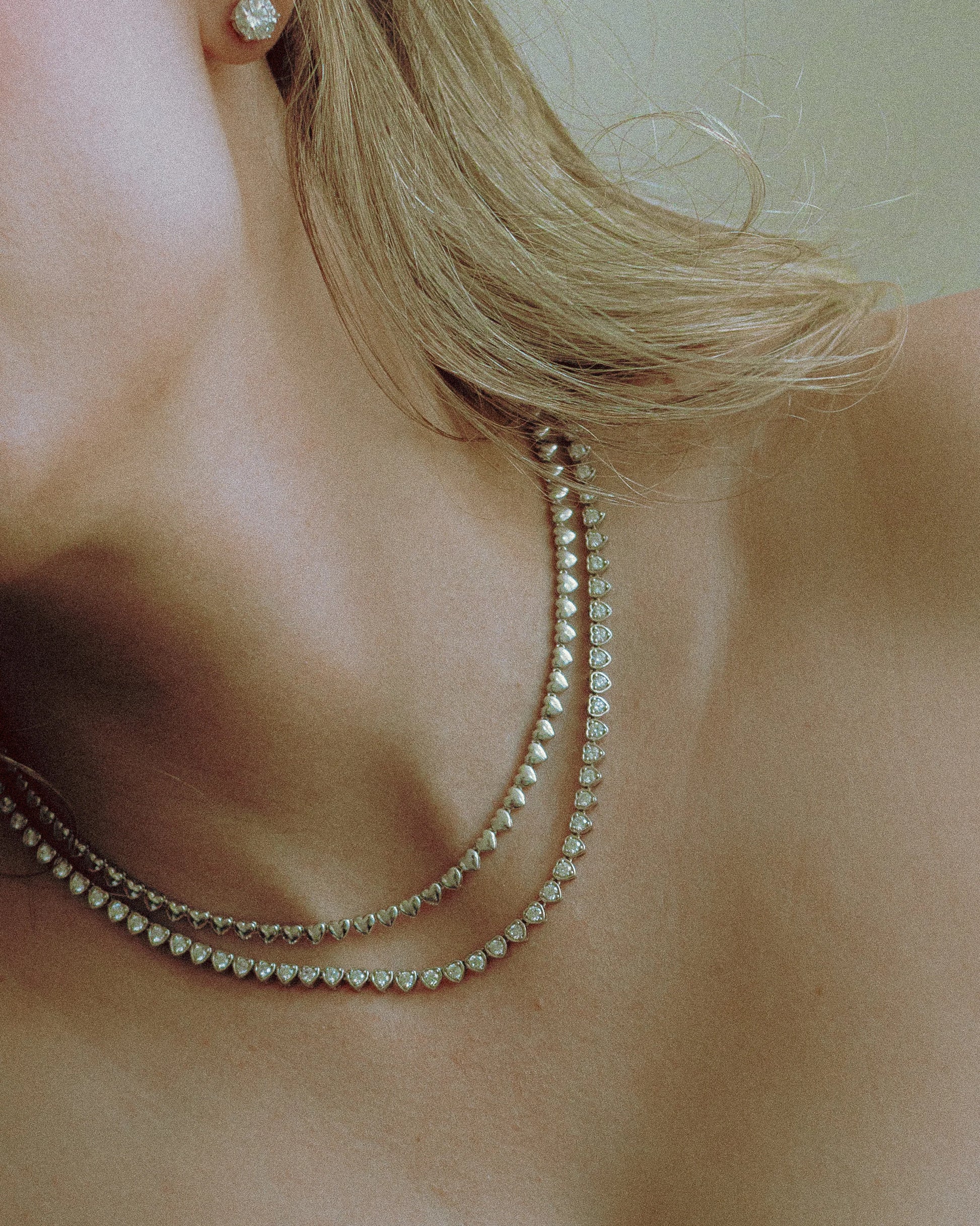 Lover’s Line Necklace by Goldmacher – Rhodium plated heart-shaped zirconia tennis necklace shown in close-up on model
