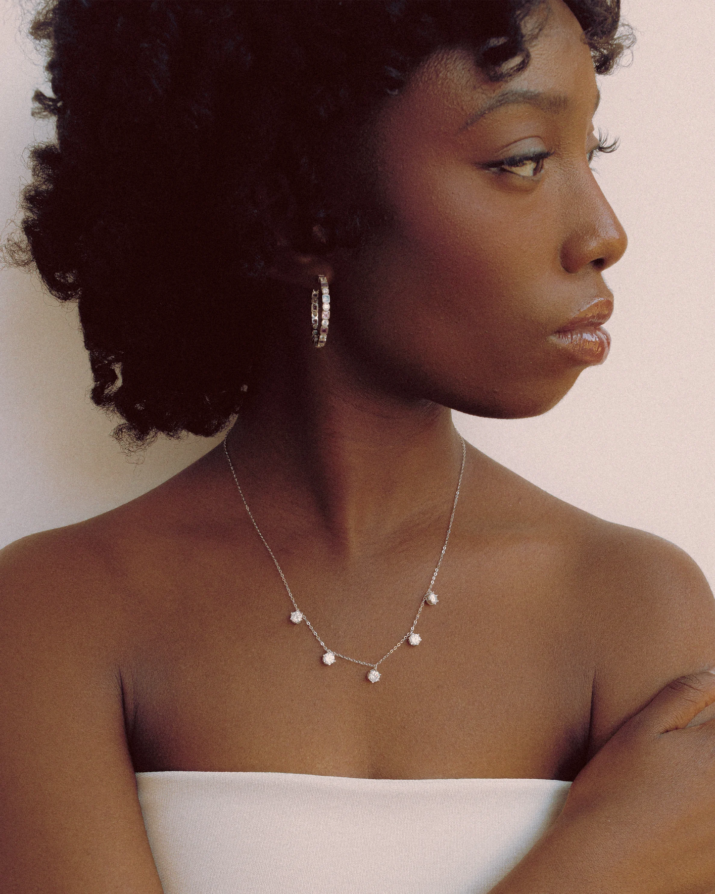Model wearing Goldmacher Prism Loop colorful zircon hoop earrings and a moissanite charm necklace in a clean, minimalist portrait