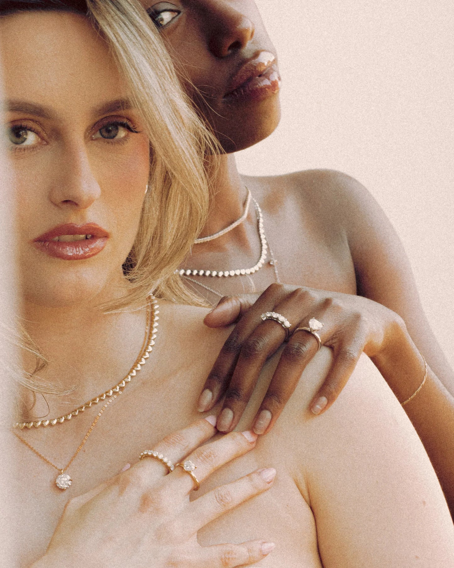 Close-up of Rigel, Elora 1CT, Elora 2CT, and Mensa moissanite rings by Goldmacher styled on two models with layered necklaces