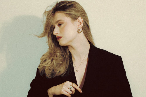 Model wearing Goldmacher Double Deluxe earrings, Bold Dome ring, and a delicate pendant necklace – styled in a minimal black look