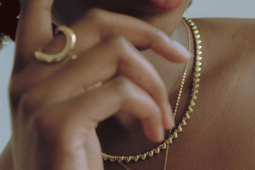  Close-up of model’s hand and neck adorned with Goldmacher Heart String Necklace and Bold Dome Ring in 18K gold – layered and elegant