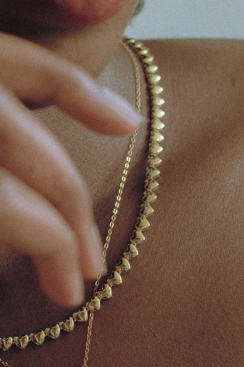  Minimalist styling detail: Goldmacher Bold Dome Ring and Heart String Necklace in 18K gold layered over bare skin