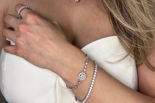 Close-up of Goldmacher moissanite heart stud earrings with a tennis necklace sparkling around the model’s neck and bracelet Mobile